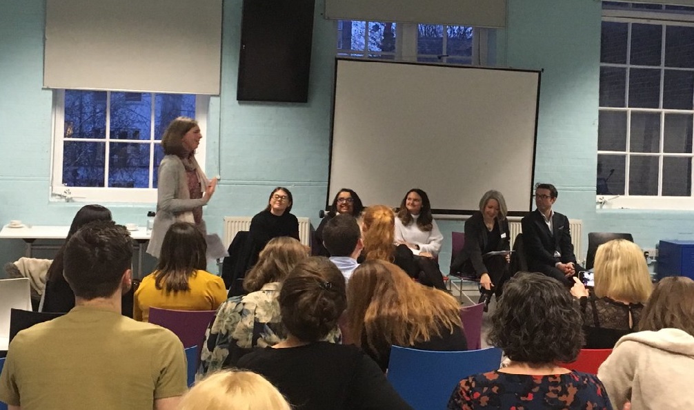 A picture of an event with people sitting in chairs and listening to speakers