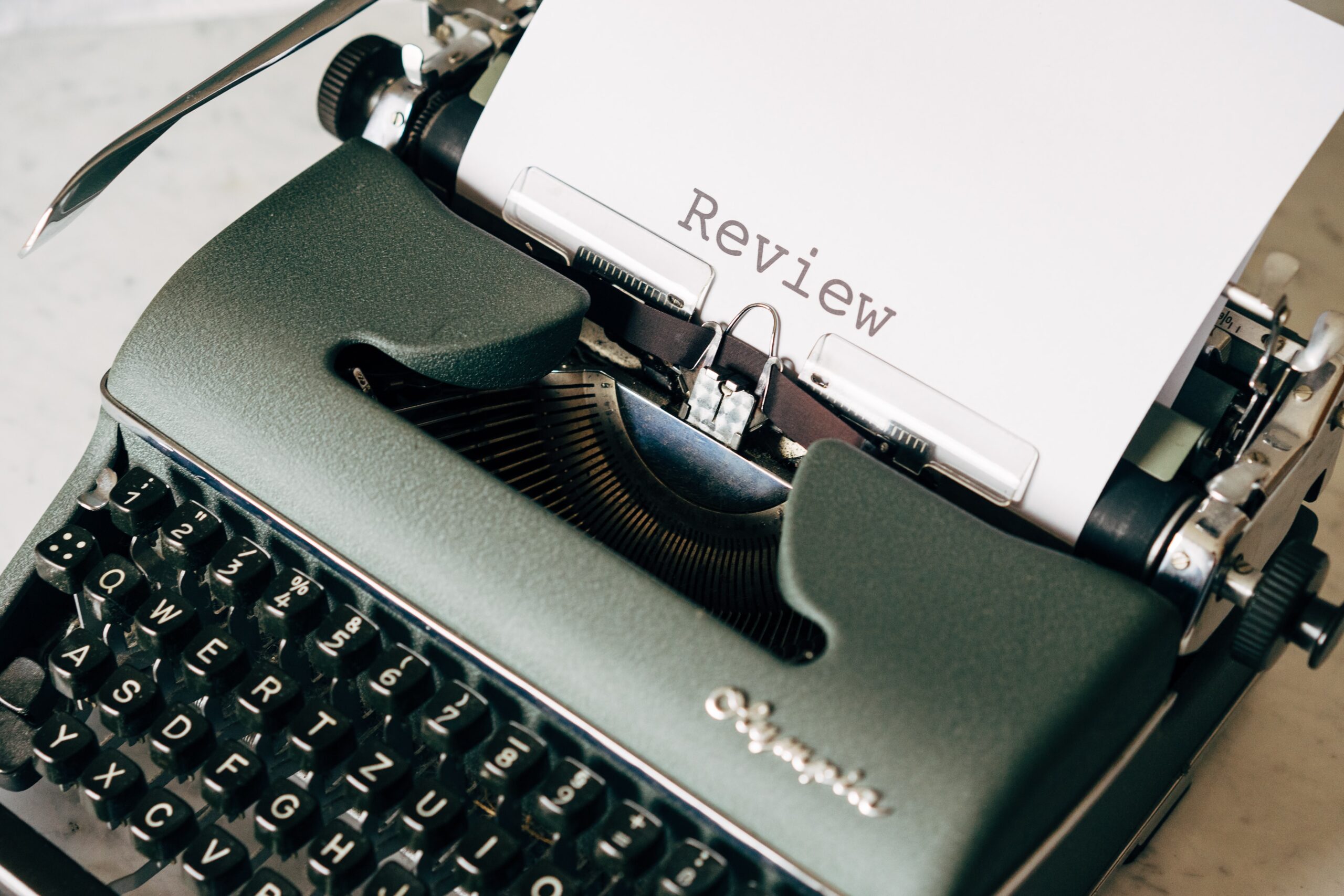 A photo of an old-fashioned typewriter with a piece of paper coming out of the top with the word review typed across it