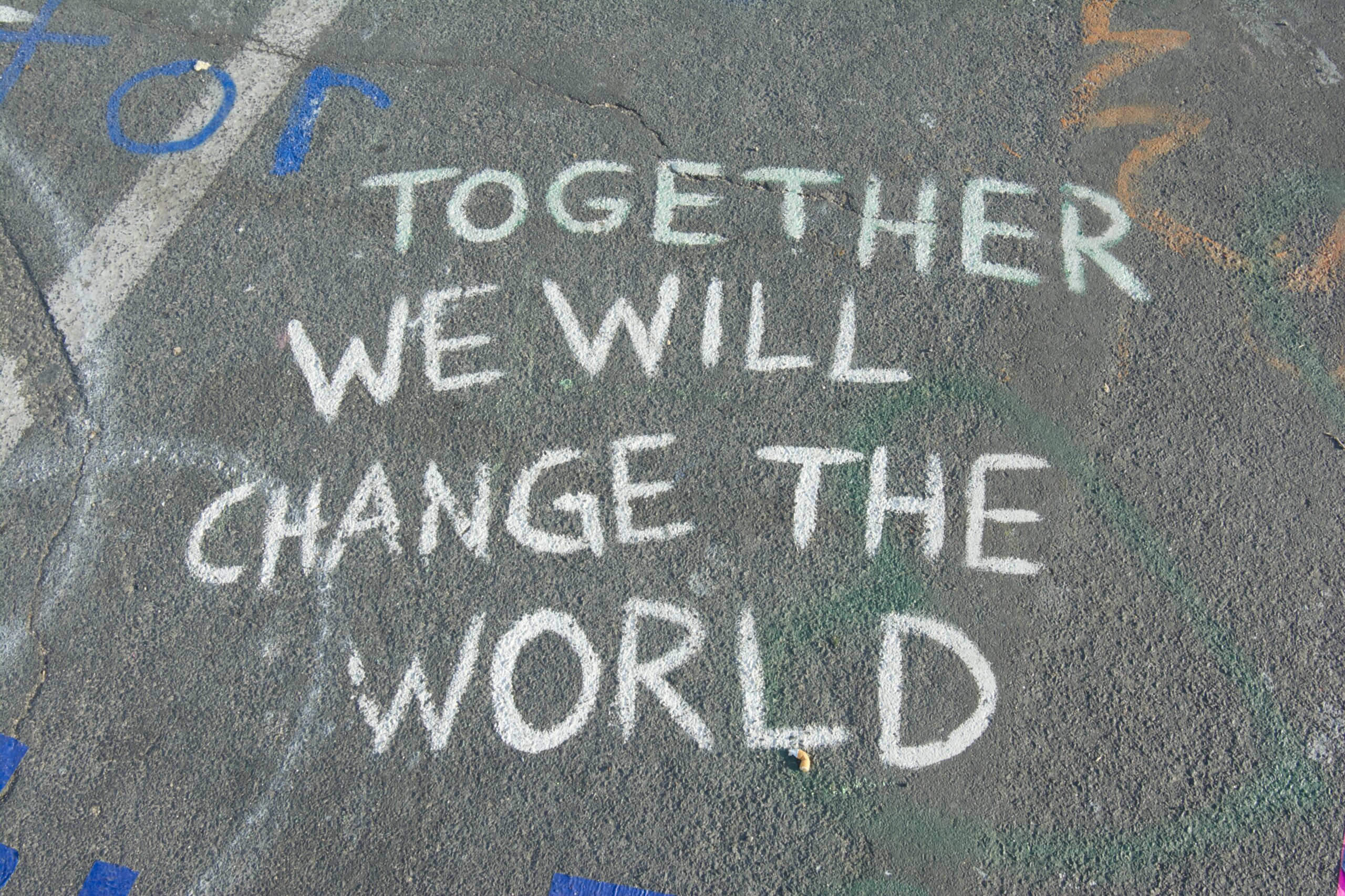 The words together we will change the world written in white chalk on a grey playground floor