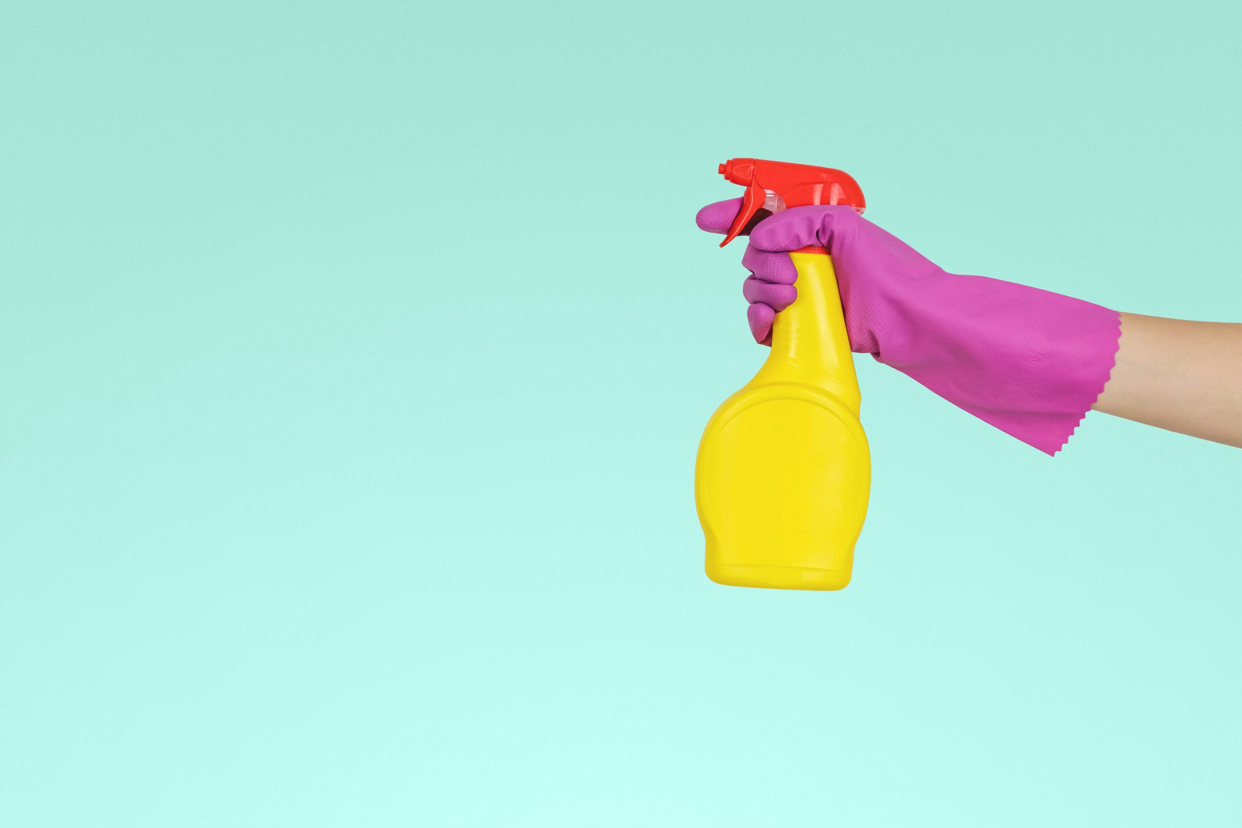 A photo of a hand in a pink rubber glove holding a yellow bottle of cleaning fluid and spraying it from right to left